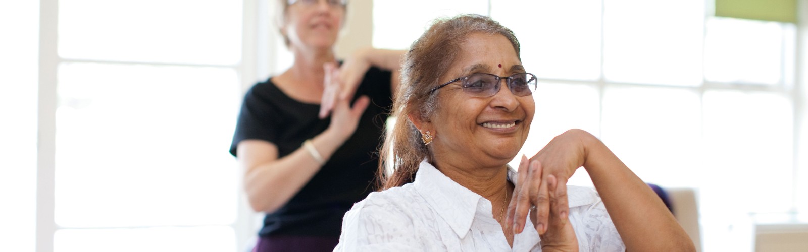 An older Asian lady smiling as she takes part in an ϲʿֱexercise class